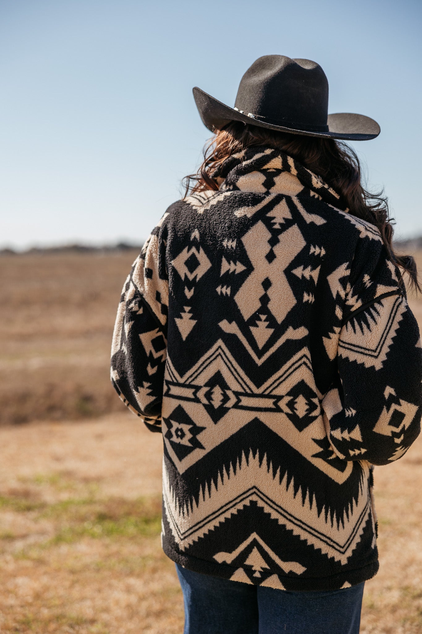 Woman in a black wide-brim hat and western aztec print jacket outdoors
