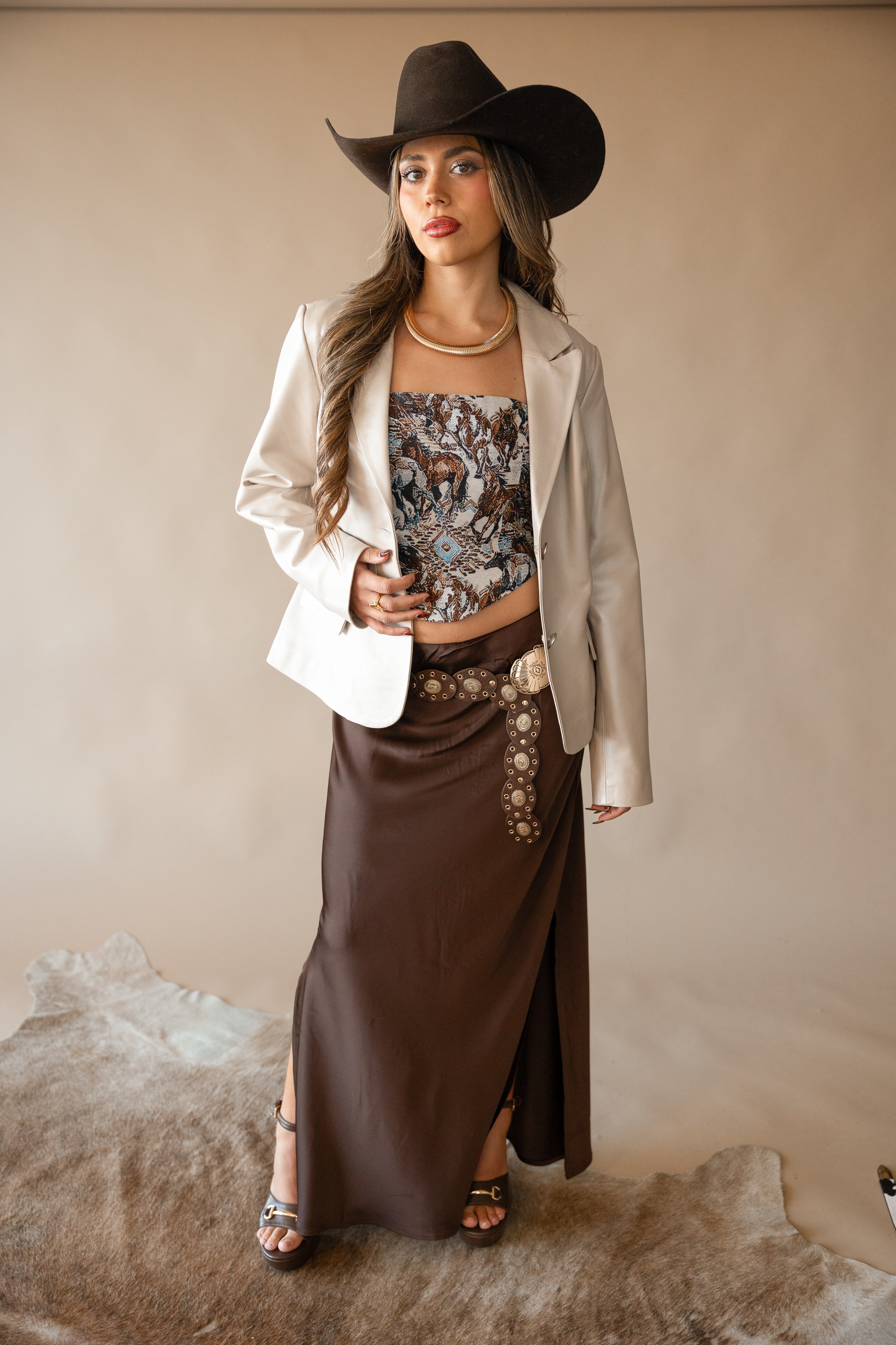 Woman in western boho outfit with cowboy hat, cream blazer, printed corset top, and brown skirt