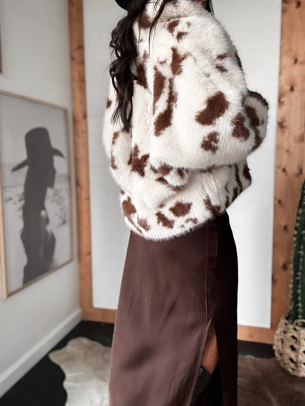 Person wearing a cow print sweater in a room with framed pictures on the wall.
