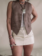 Woman in western boho outfit with brown checkered vest, leather mini skirt, and statement jewelry