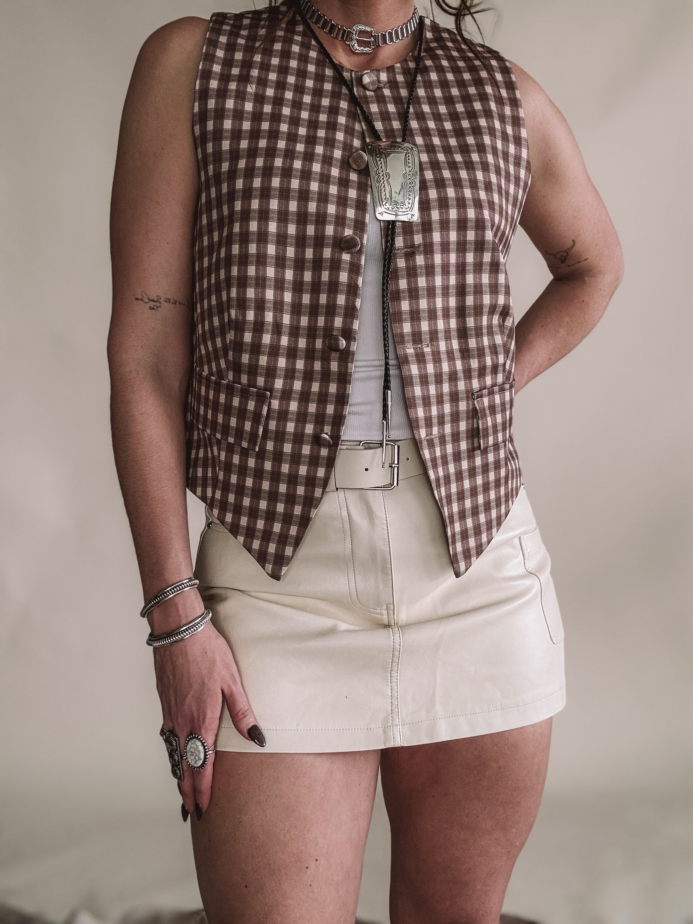 Woman in western boho outfit with brown checkered vest, leather mini skirt, and statement jewelry