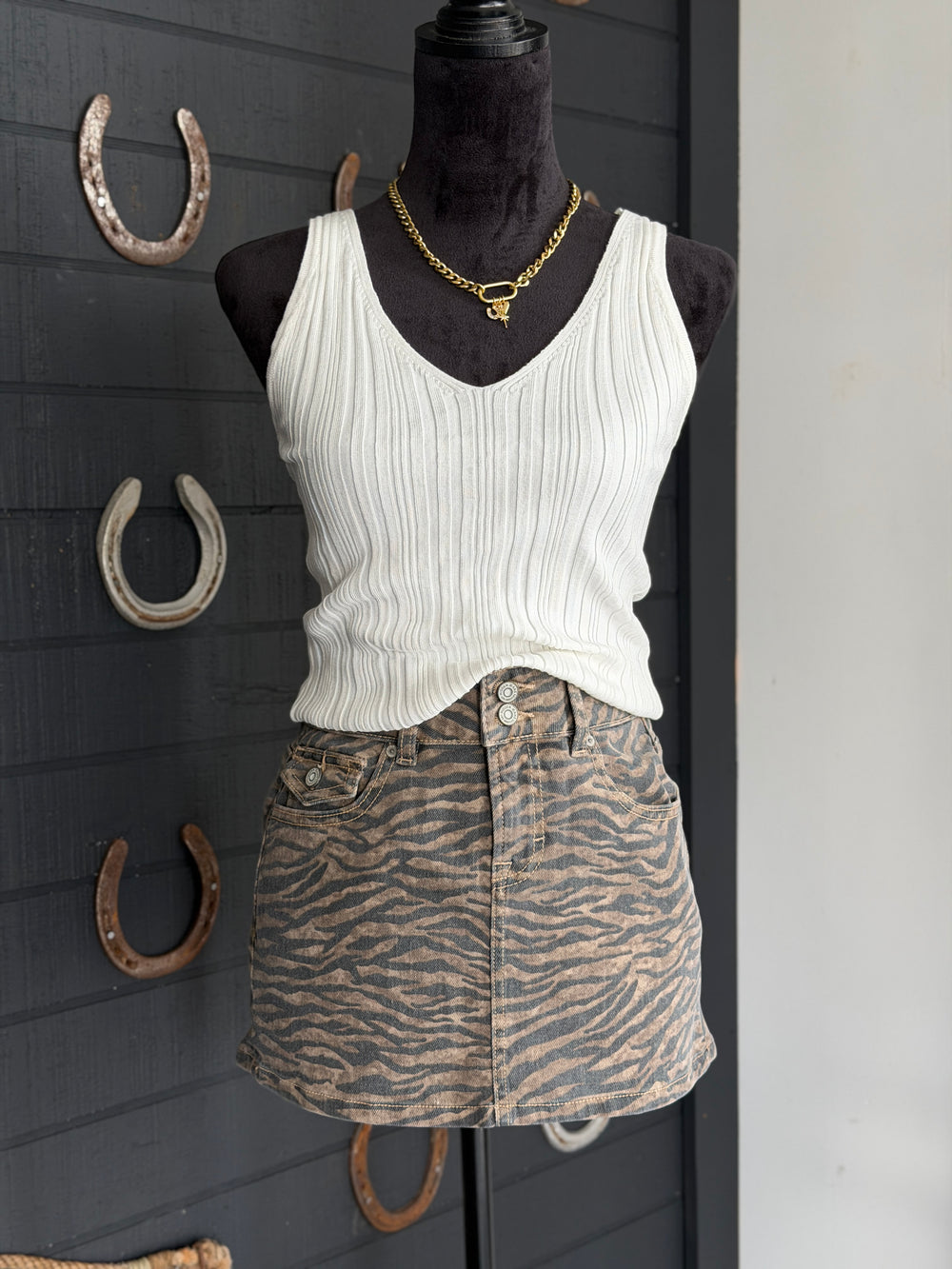 Mannequin wearing a white tank top and zebra print skirt with horseshoe decorations on a dark wall.