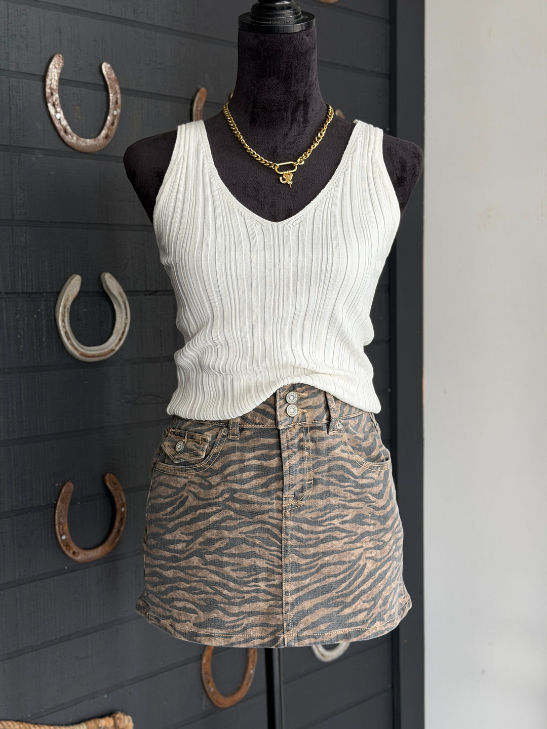 Mannequin wearing a white tank top and zebra print skirt with horseshoe decorations on a dark wall.