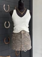 Mannequin wearing a white tank top and zebra print skirt with horseshoe decorations on a dark wall.