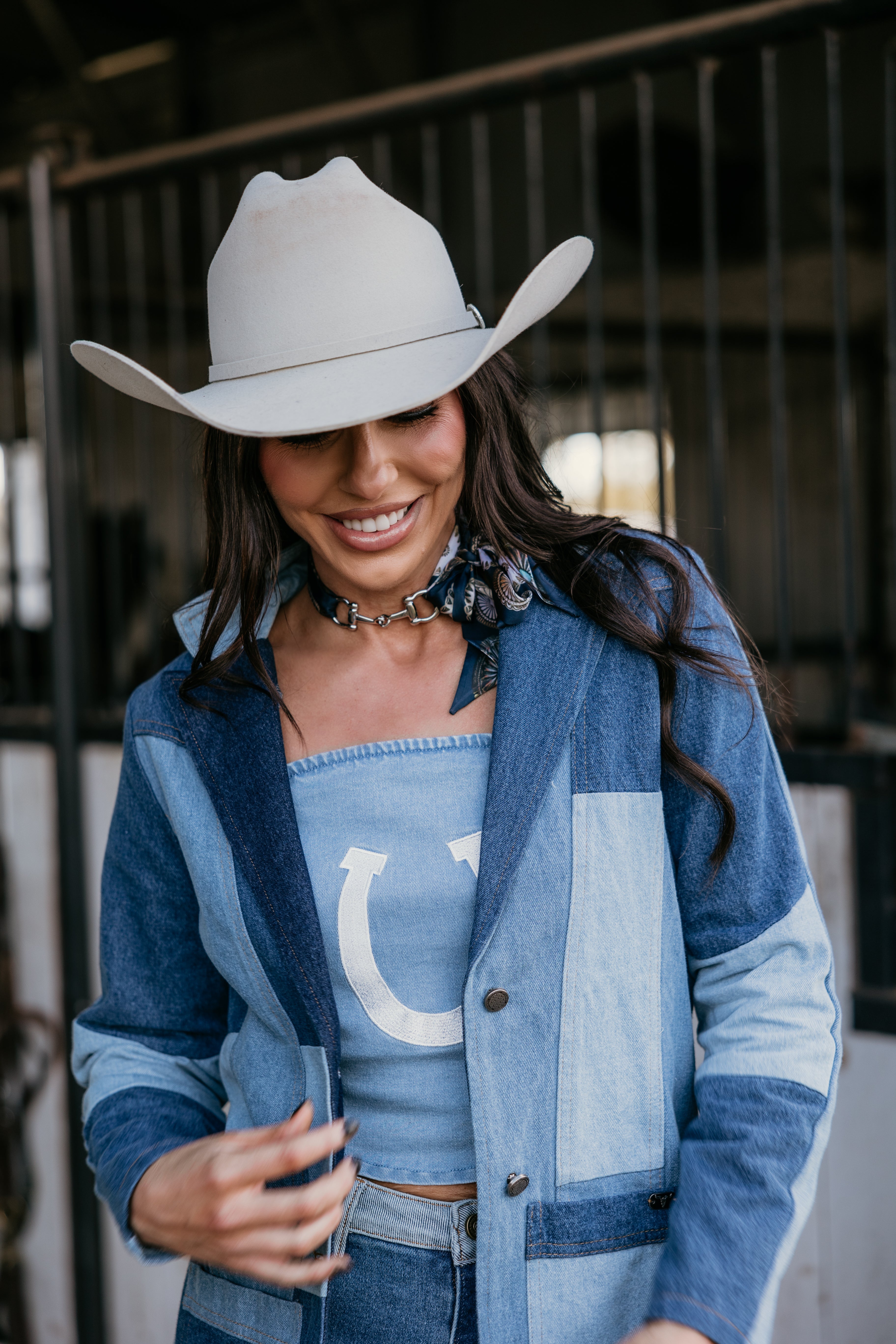 Smiling woman in western boho denim jacket, light blue tube top, and white cowgirl hat