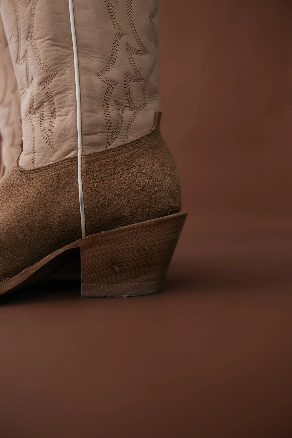 Close-up of a brown cowboy boot with detailed stitching on a brown background