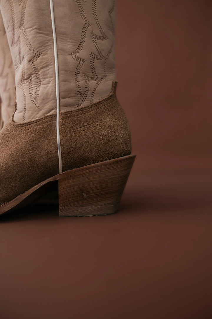 Close-up of a brown cowboy boot with detailed stitching on a brown background