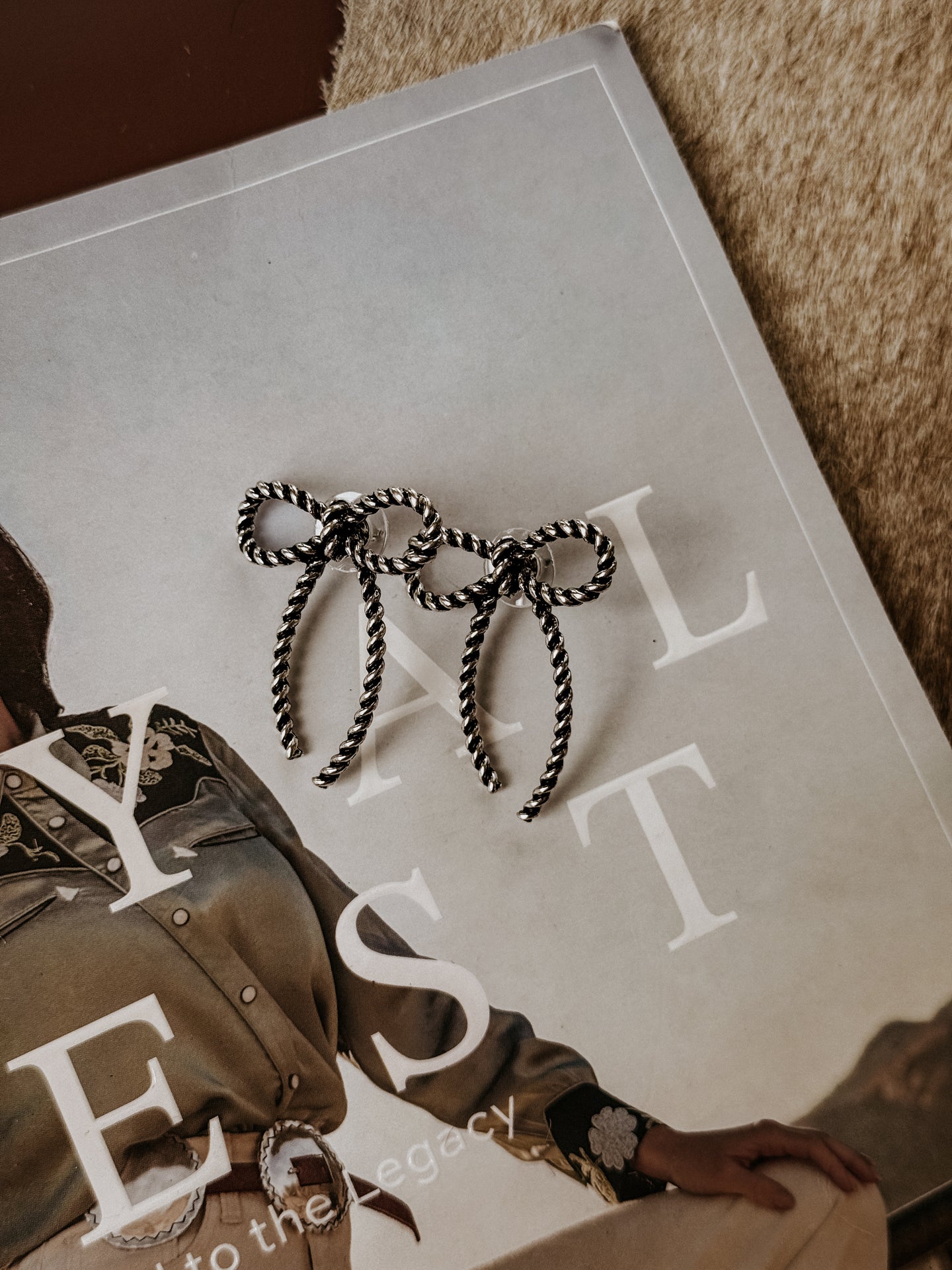 Burnished silver earrings with a twisted rope bow design, lightweight construction, and post back closure. Feminine western-inspired statement piece suitable for everyday wear or special occasions.