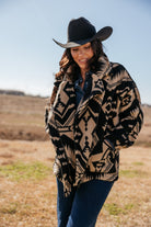 Woman in western boho Aztec jacket, black cowboy hat, and denim jeans outdoors