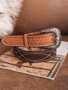 Tooled leather western belt with silver buckle on a cowboy-themed magazine, rustic setting.