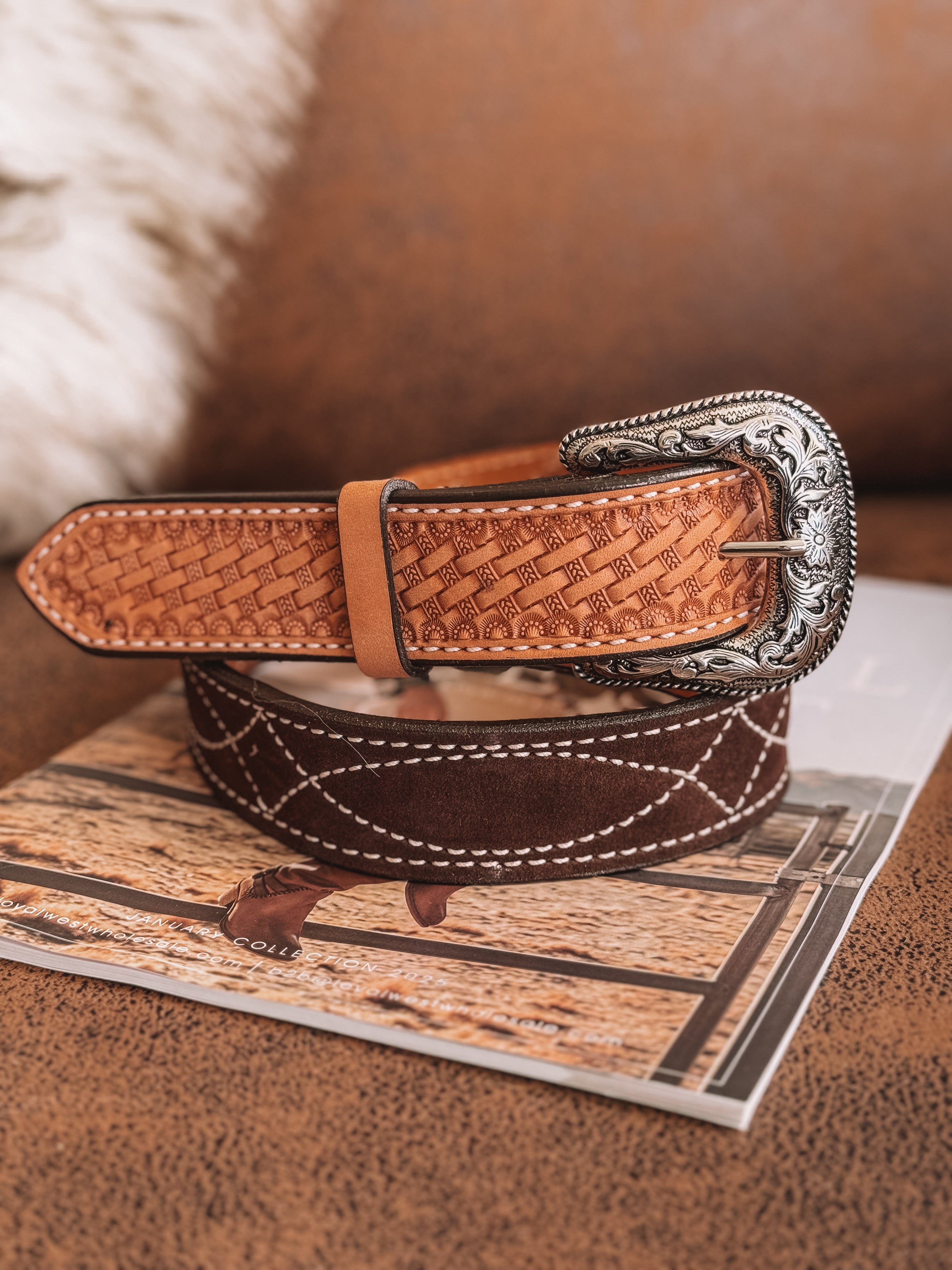 Tooled leather western belt with silver buckle on a cowboy-themed magazine, rustic setting.