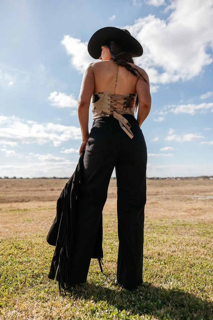 Woman in western boho outfit with black wide-leg pants, corset top, and cowboy hat outdoors