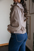 Woman wearing brown gingham ruffle blouse and high-waisted blue jeans, western style