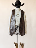 Western cowgirl outfit with felt hat, knit sweater, brown leather vest, cow print skirt, necklace, and cowboy boots