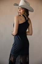 Woman in black fringe western dress with white cowboy hat, looking over shoulder