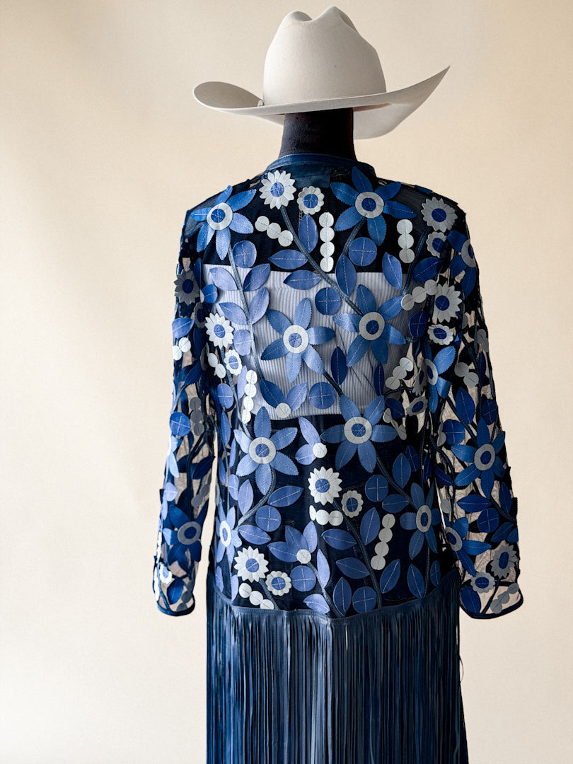Woman in white cowboy hat wearing sheer blue floral fringe western jacket, back view