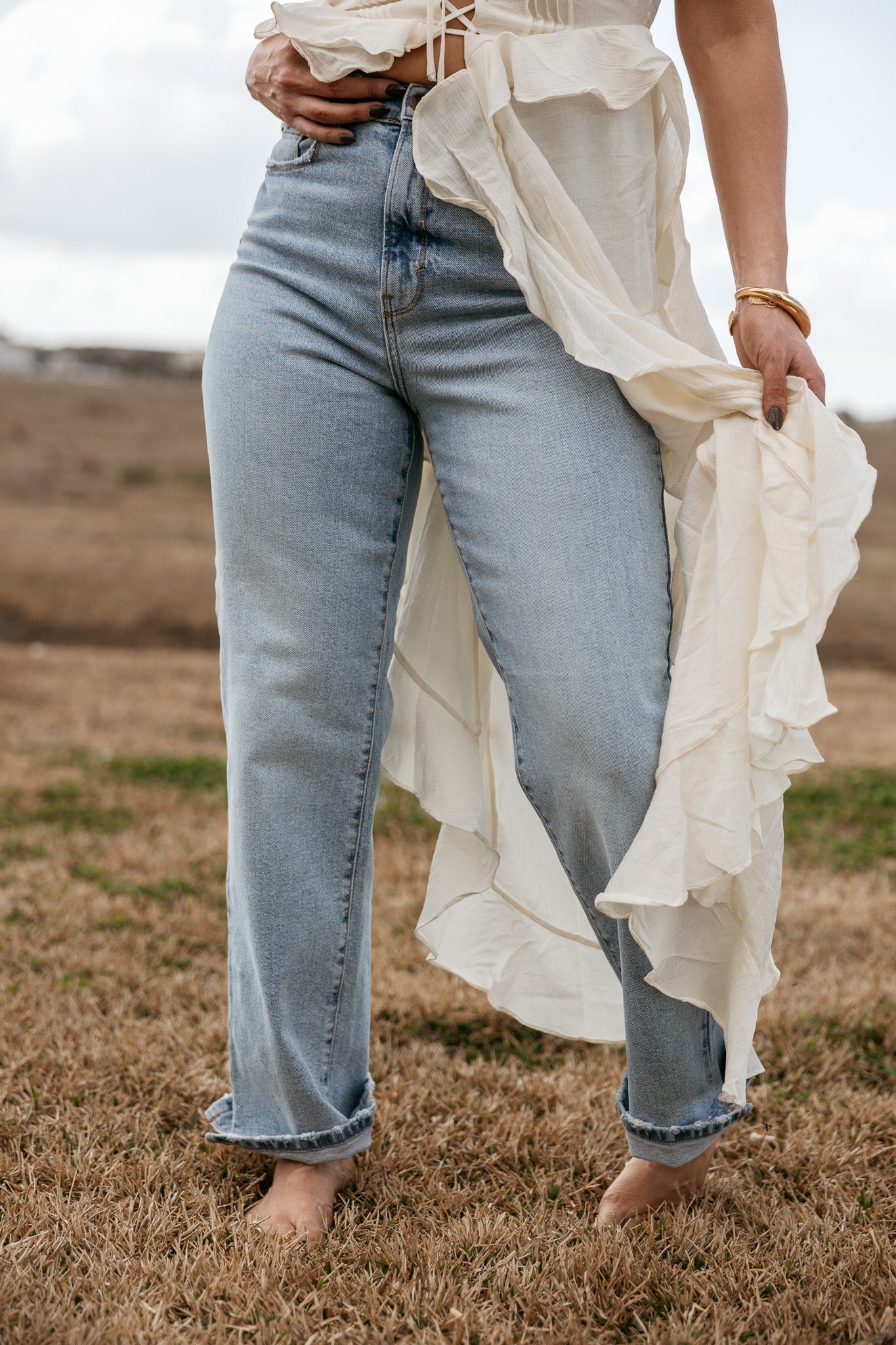 Woman in light wash western jeans and flowy white boho top standing barefoot on grass