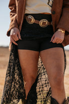 Western boho outfit with black lace skirt, gold concho belt, and brown suede jacket outdoors