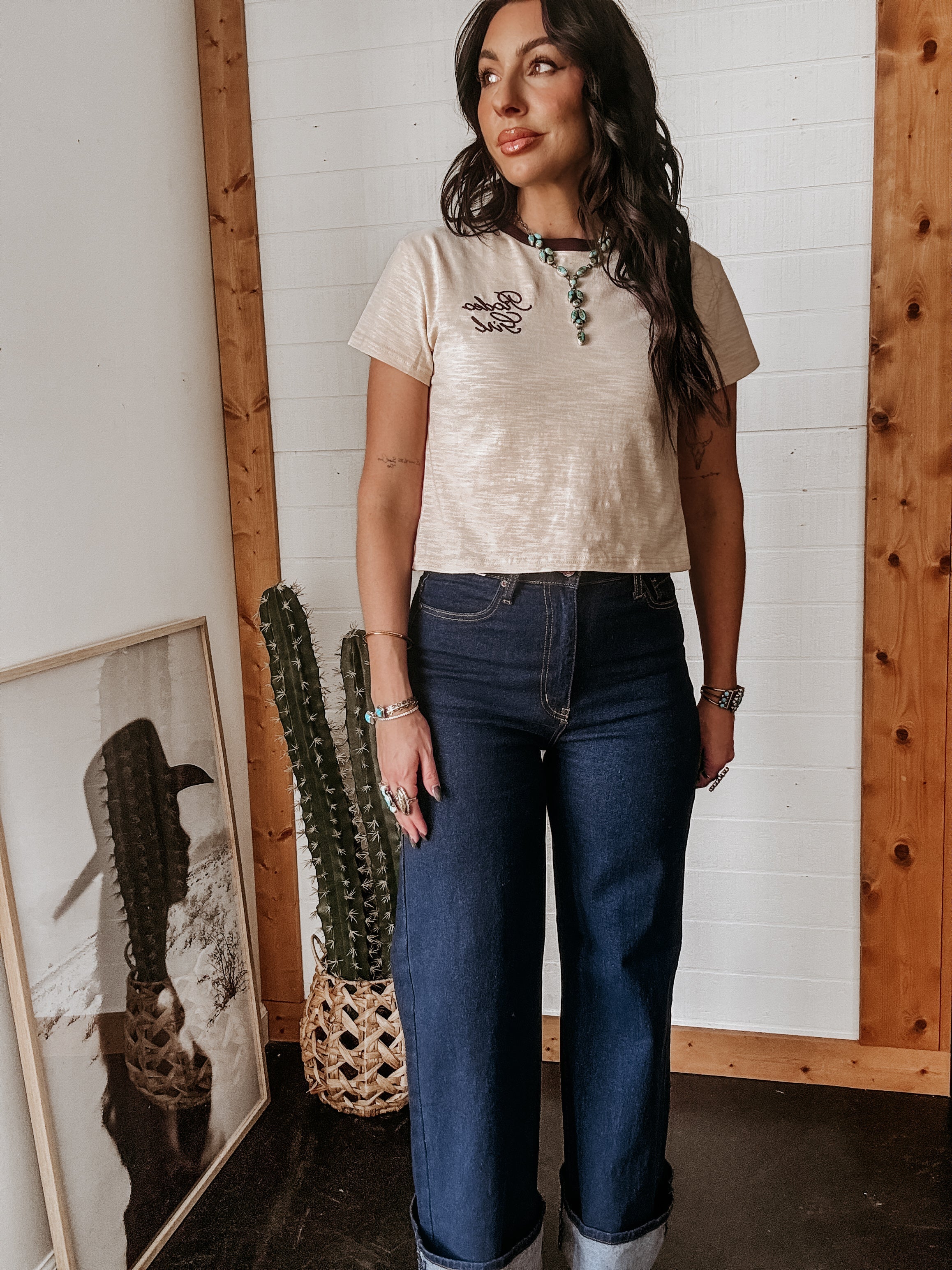 Woman in western boho outfit with graphic tee, turquoise jewelry, and wide leg jeans