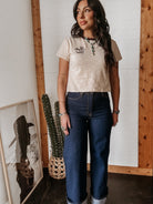 Woman in western boho outfit with graphic tee, turquoise jewelry, and wide leg jeans