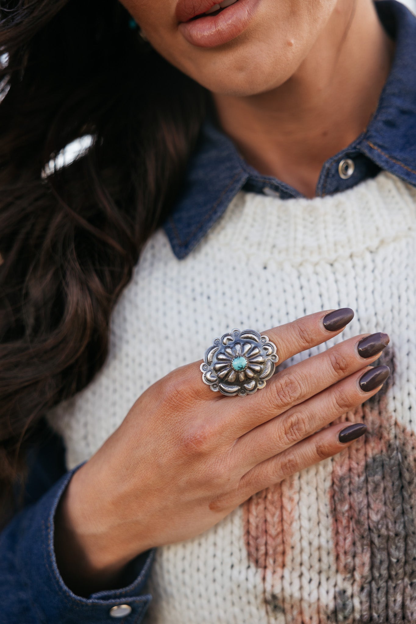 Woman wearing western silver statement ring with turquoise stone, denim shirt, and knit sweater