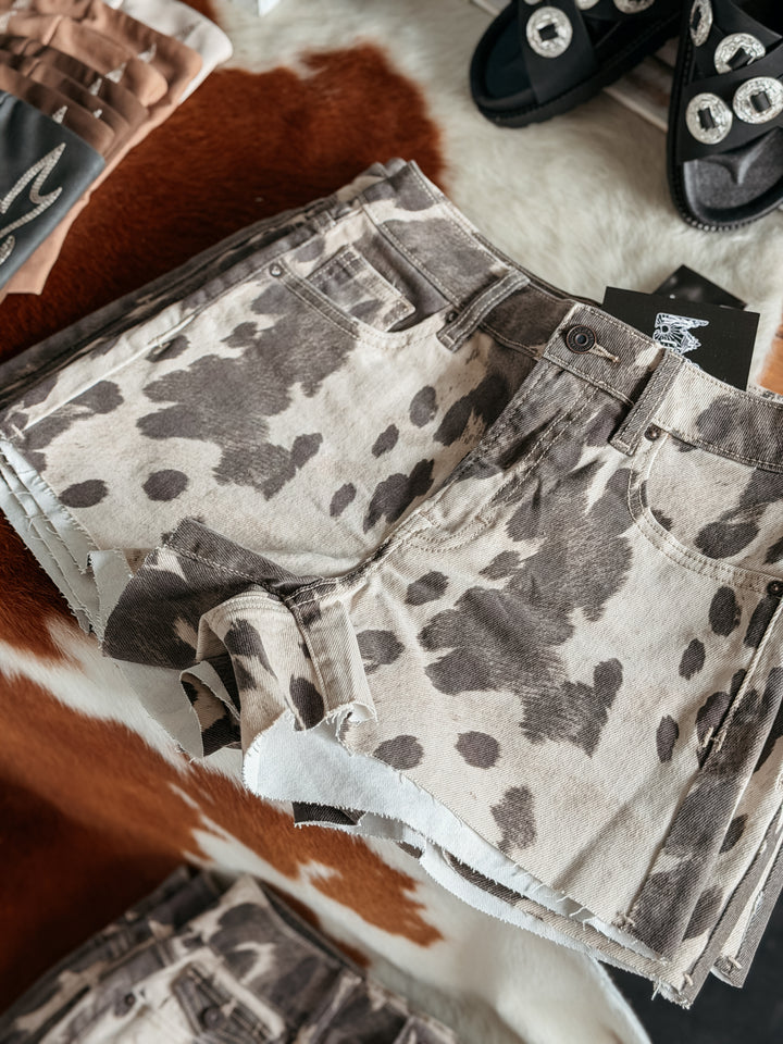 Cow print shorts on a textured surface with shoes in the background