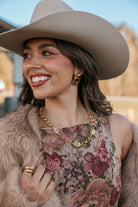 Woman in cowgirl hat, floral western dress, gold jewelry, and faux fur jacket outdoors