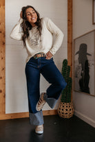 Woman in western boho outfit wearing graphic saddle up sweater and wide-leg jeans indoors