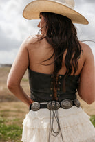 Woman in western boho outfit with cowboy hat, lace skirt, concho belt, and corset top outdoors