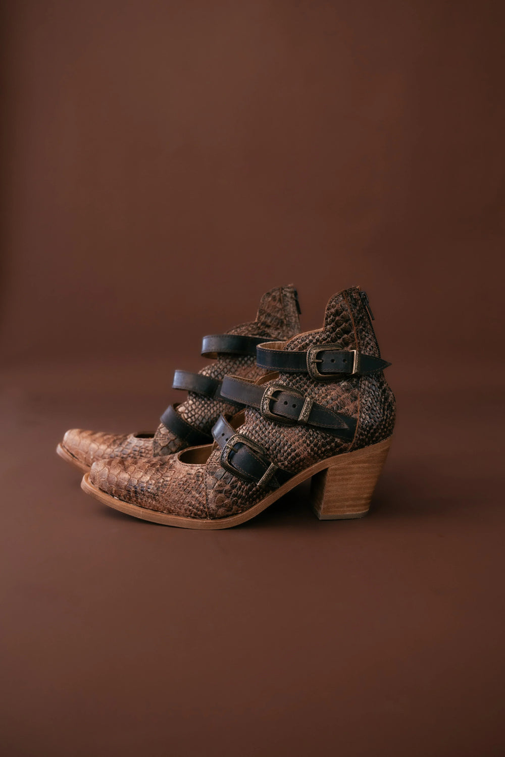 Pair of brown patterned shoes with wooden soles on a brown background