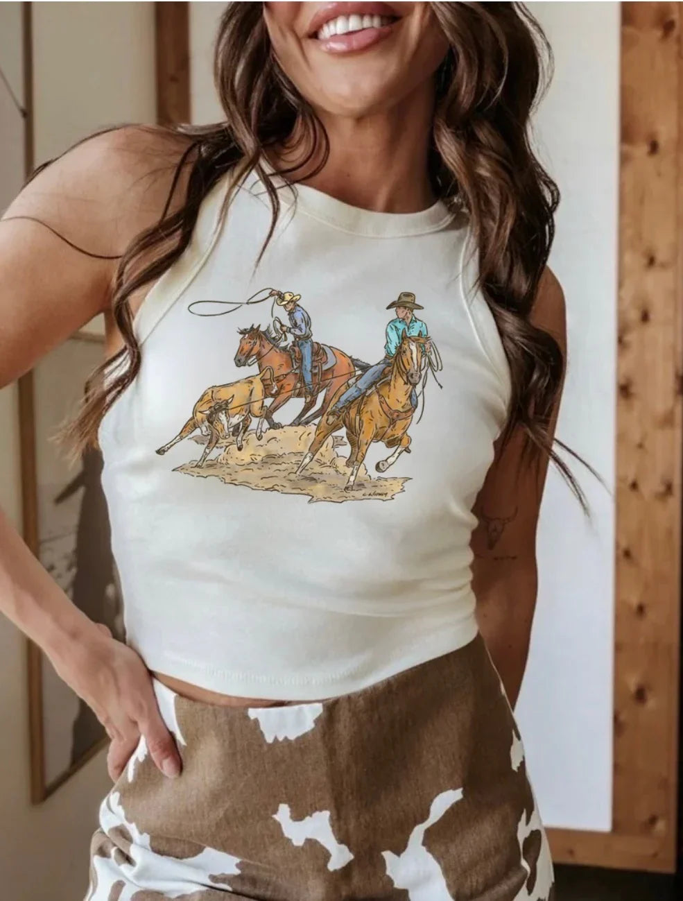 Woman wearing a sleeveless top with a graphic of cowboys on horses.