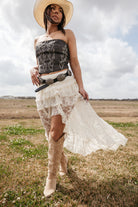 Woman in western boho outfit with lace skirt, cowboy boots, wide belt, and straw hat outdoors