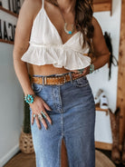 Woman in western boho outfit with white ruffle crop top, denim skirt, turquoise jewelry