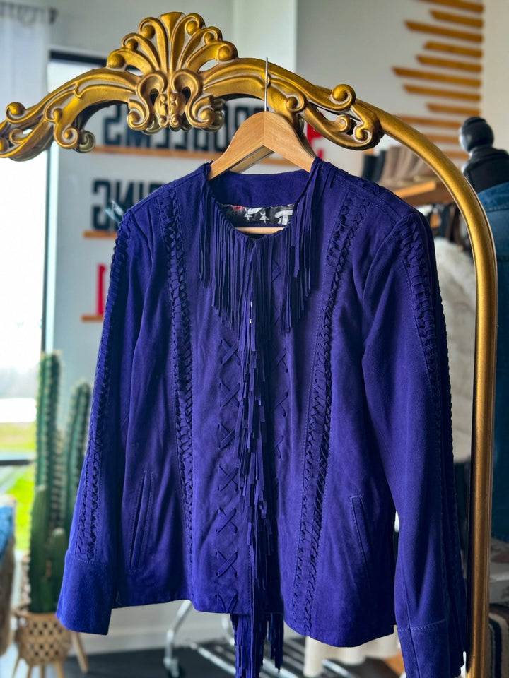 Purple suede western jacket with fringe and braided details on a hanger, boutique setting.