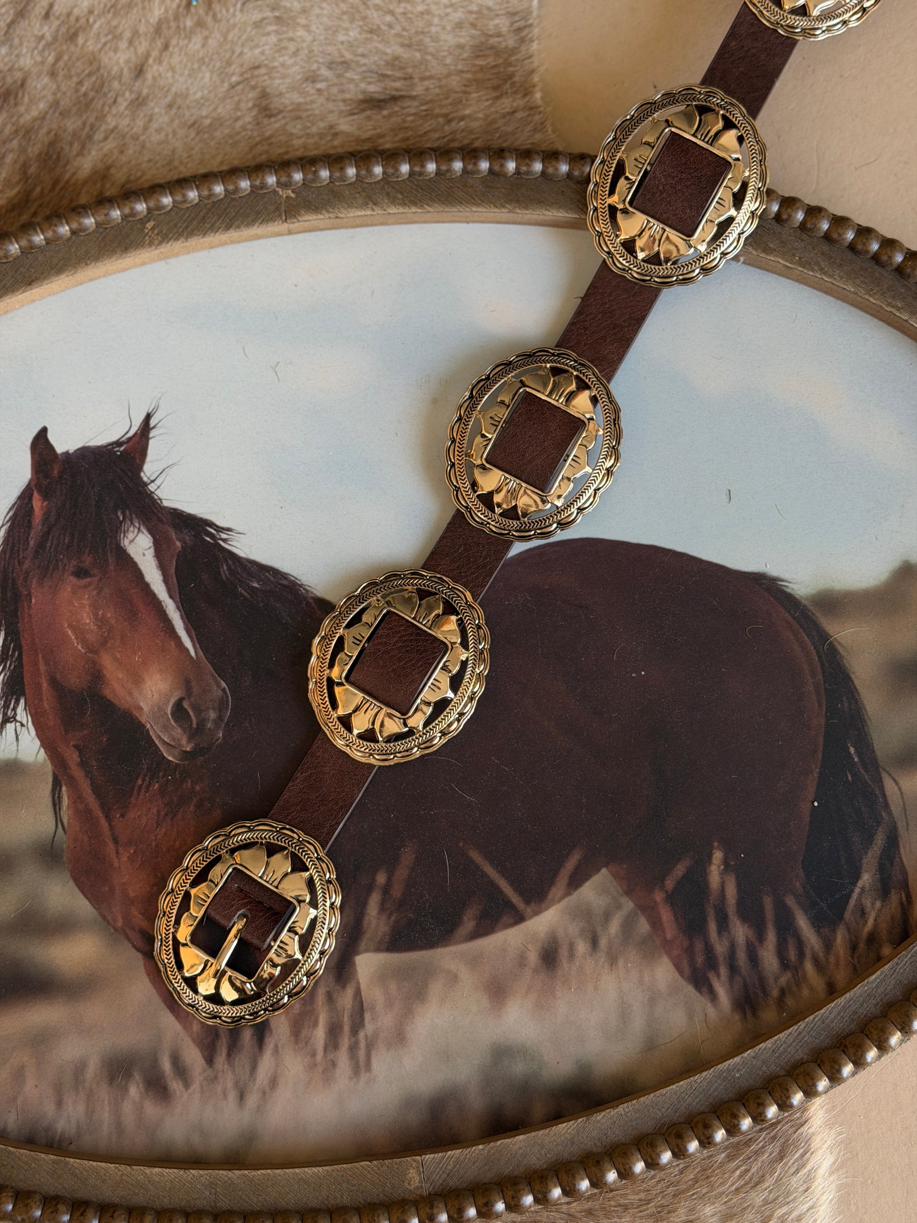 Western concho belt with engraved gold accents on brown leather, rustic cowgirl style