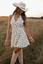 Woman in a floral dress and cowboy hat standing in a field.