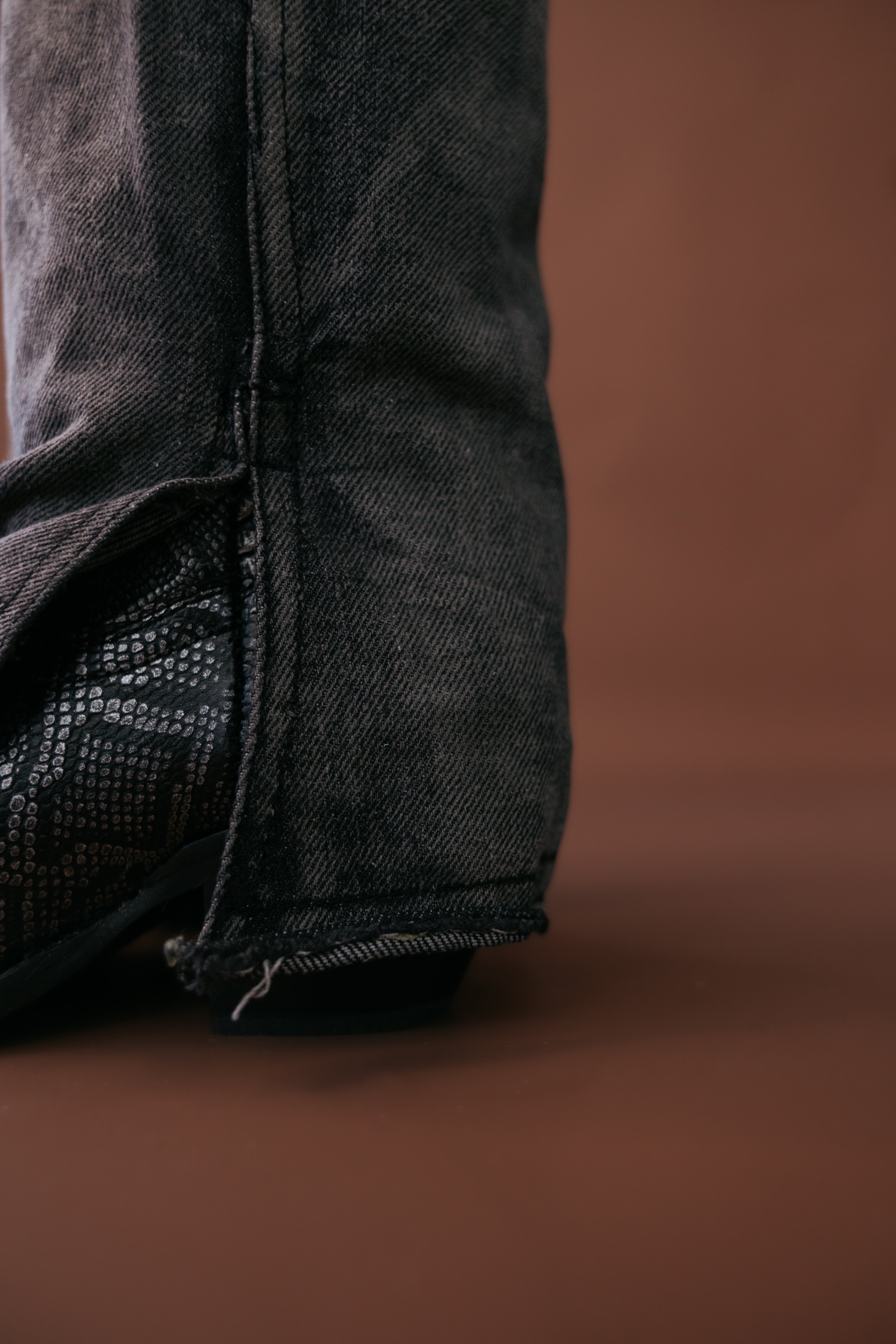 Black denim jeans with raw hem over black western boot on brown background