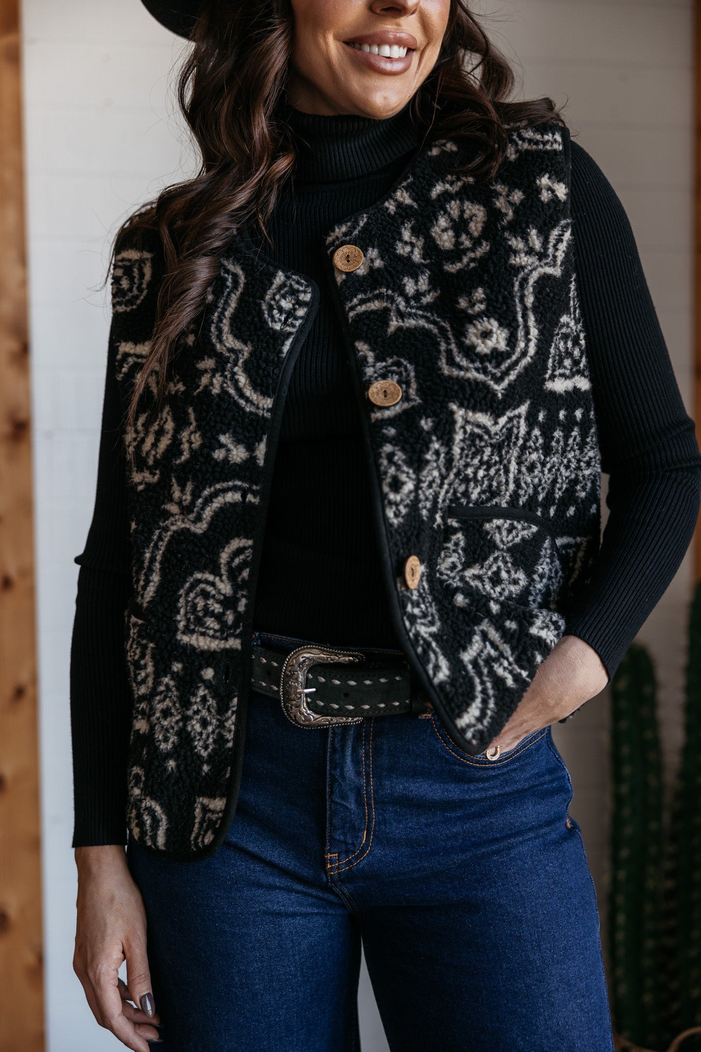 Woman in western boho patterned vest, black turtleneck, and high-rise blue jeans