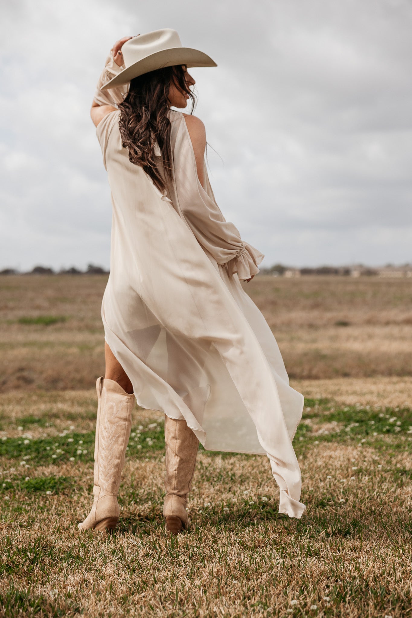 Woman in beige western boho dress and cowboy boots posing in a grassy field