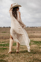 Woman in beige western boho dress and cowboy boots posing in a grassy field