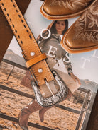 Western cowgirl boots and tooled belt buckle on a magazine with a rodeo outfit model