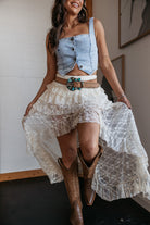 Woman in western boho outfit with denim crop top, lace skirt, turquoise belt, and cowboy boots