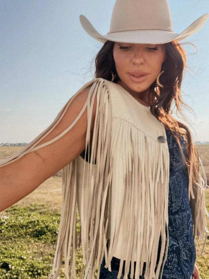 Woman in beige cowgirl hat and fringe western vest, boho rodeo style outdoors