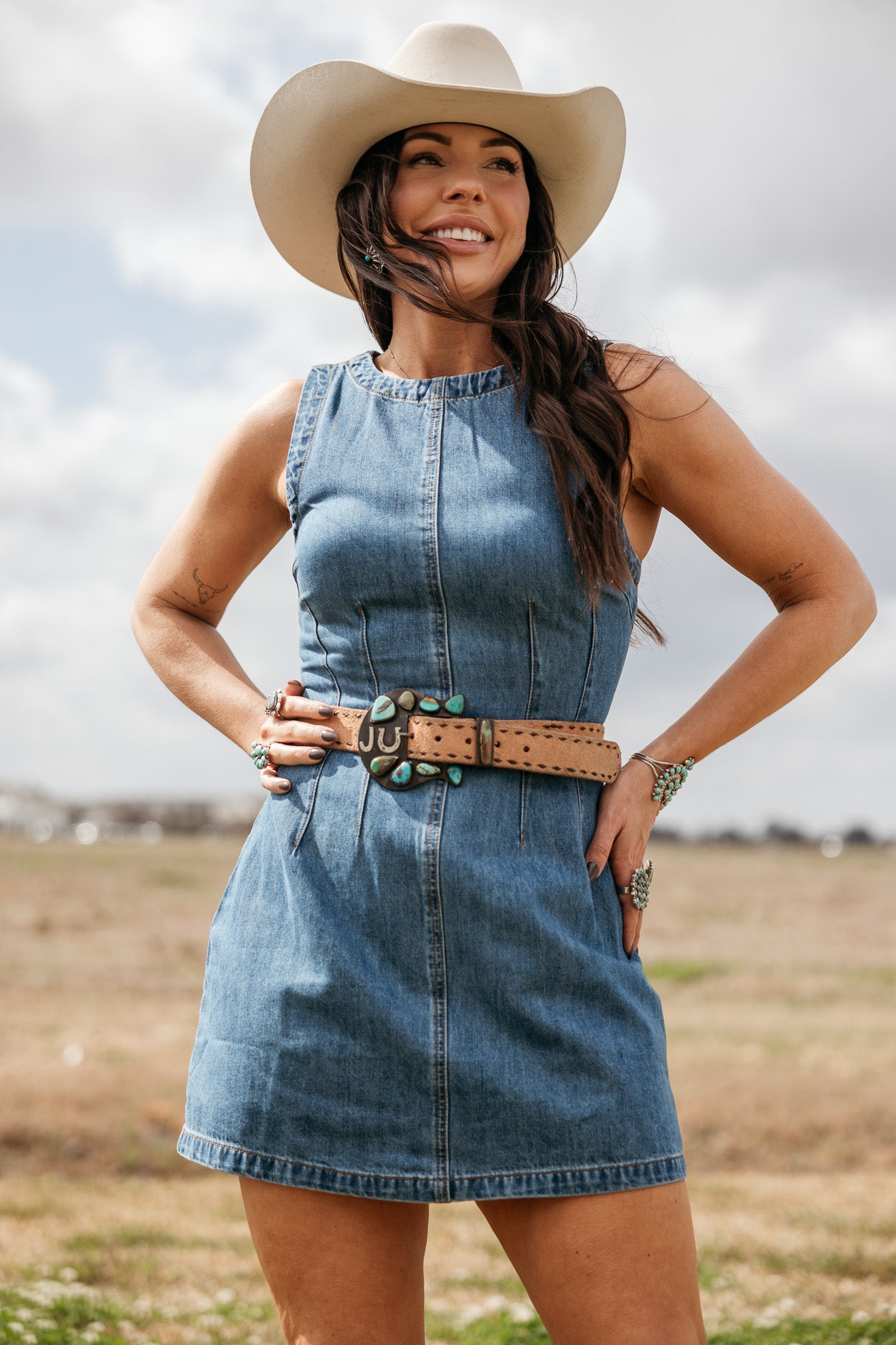 Woman in denim western dress with cowgirl hat, turquoise concho belt, and boho jewelry outdoors