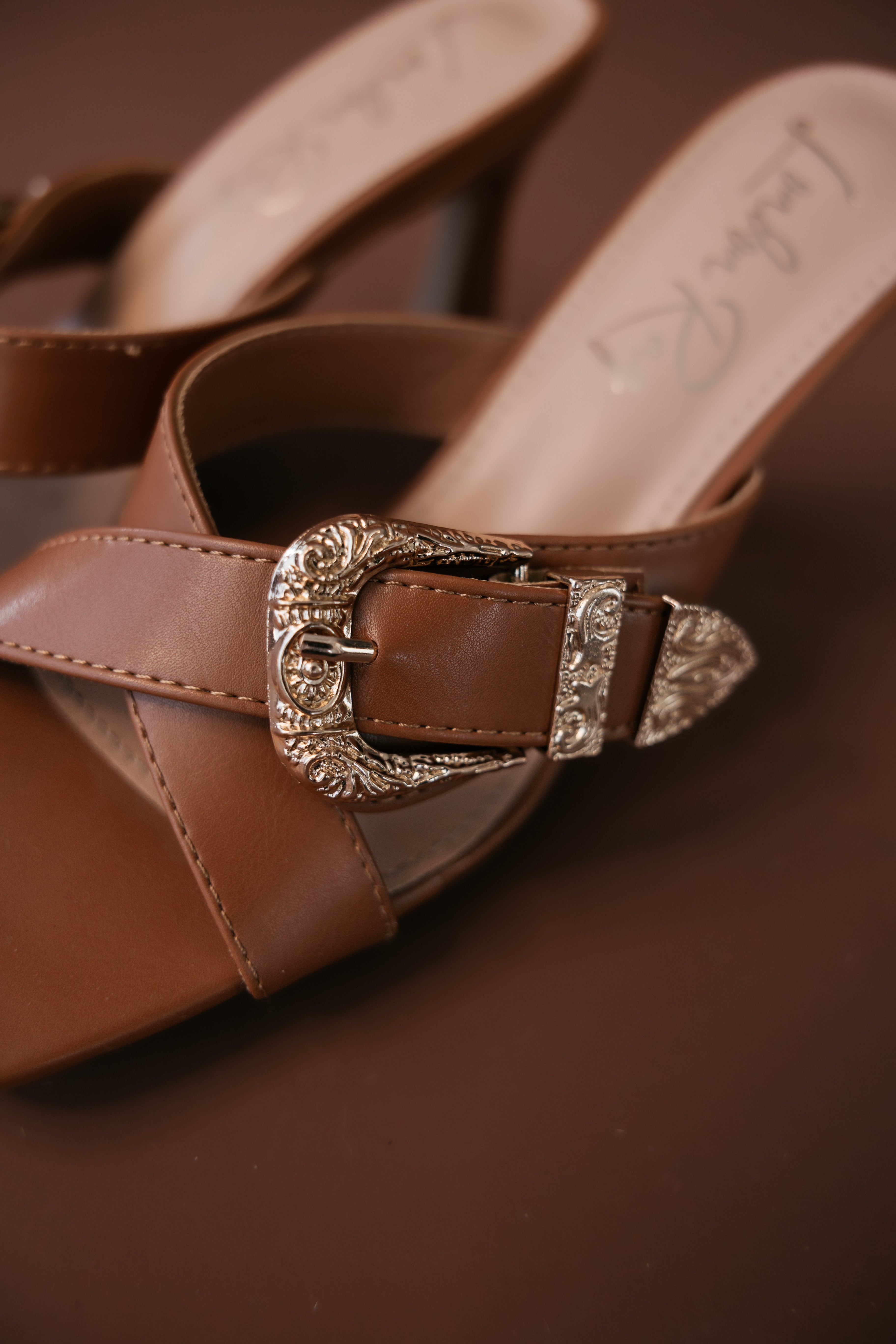 Brown western sandal with silver engraved buckle, boho cowgirl footwear on brown background