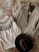 Gray checkered blazer, black and white patterned shirt, black hat, and gold necklace on a textured surface.