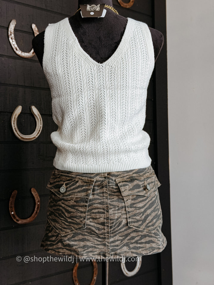 White knitted vest on a mannequin with a zebra print skirt against a dark background.