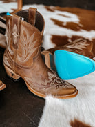 Brown embroidered western cowgirl boots with turquoise soles on cowhide rug