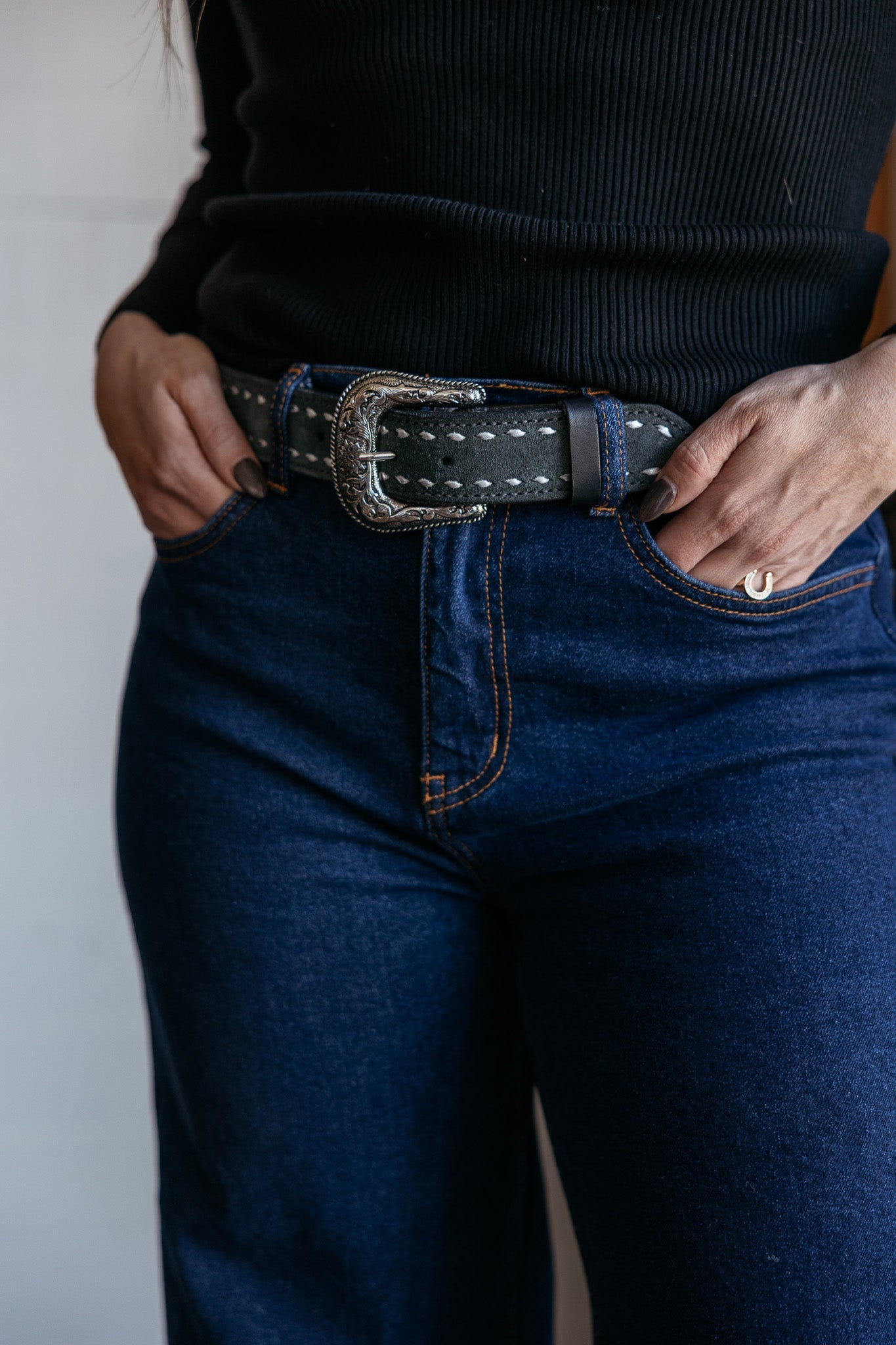 Woman wearing high-waisted blue jeans, black ribbed top, and western tooled leather belt