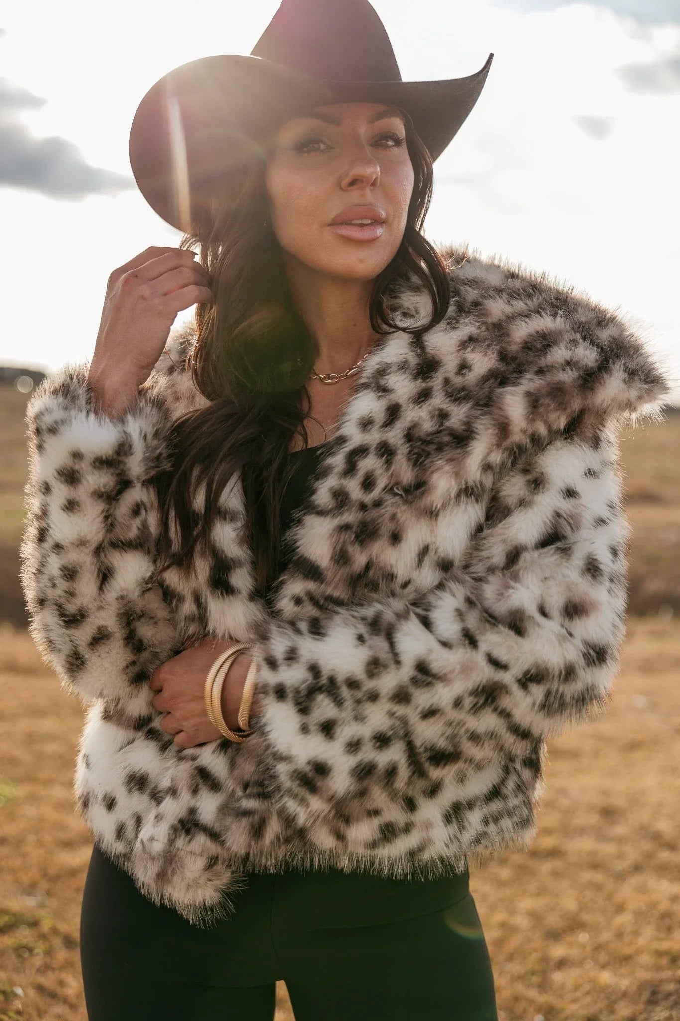 Woman in a black cowboy hat and faux fur leopard print jacket outdoors, western boho style